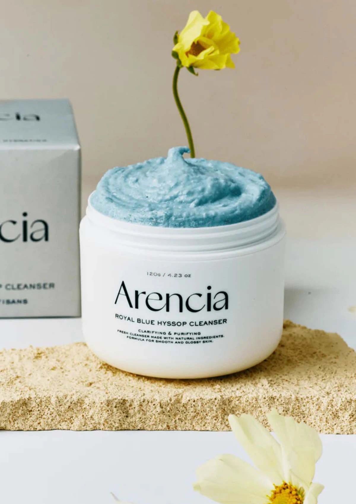 Arencia Royal Blue Hydrating Cleanser with a yellow flower on top, placed on a beige surface.